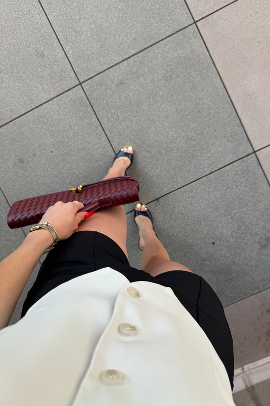 Person holding a maroon clutch on a tiled floor