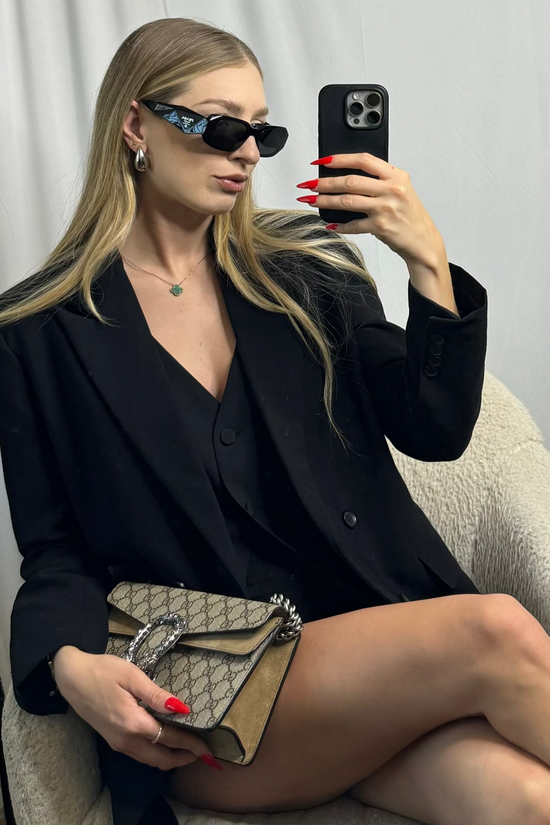 Woman in a black outfit holding a Gucci handbag, taking a mirror selfie.