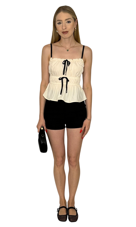 Sleeveless cami top with adjustable spaghetti straps, scoop neckline, ruched detailing, and front ribbon bow for a feminine touch