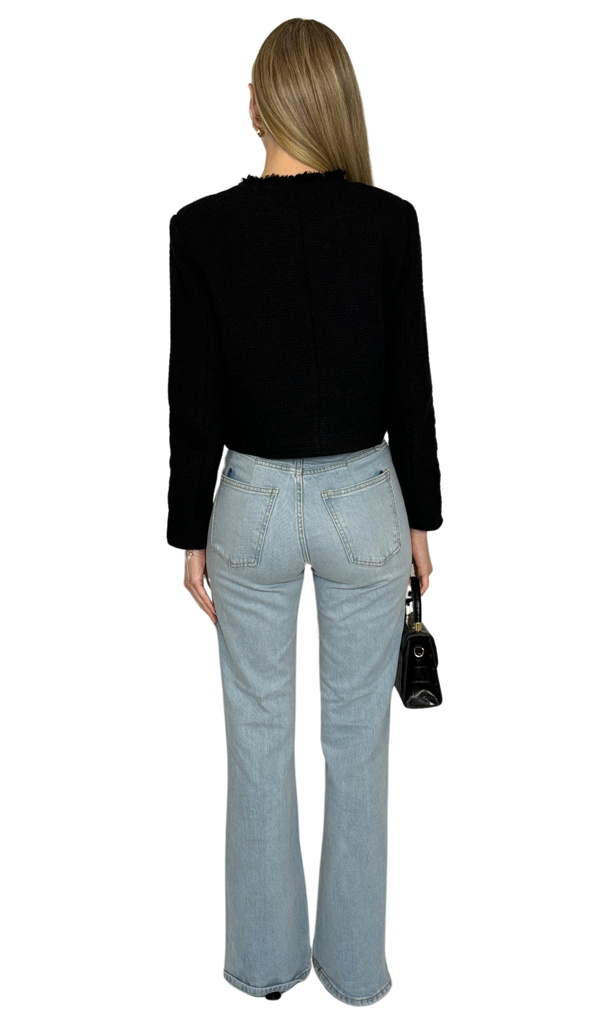 A woman wearing a tweed jacket with a mock neckline, long sleeves, and button-down closure. The jacket is black with gold buttons, and she is also wearing light blue jeans and carrying a black bag.